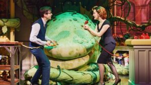 Woman holding a red phone talking to a man holding a yellow phone with a huge plant creature in the background
